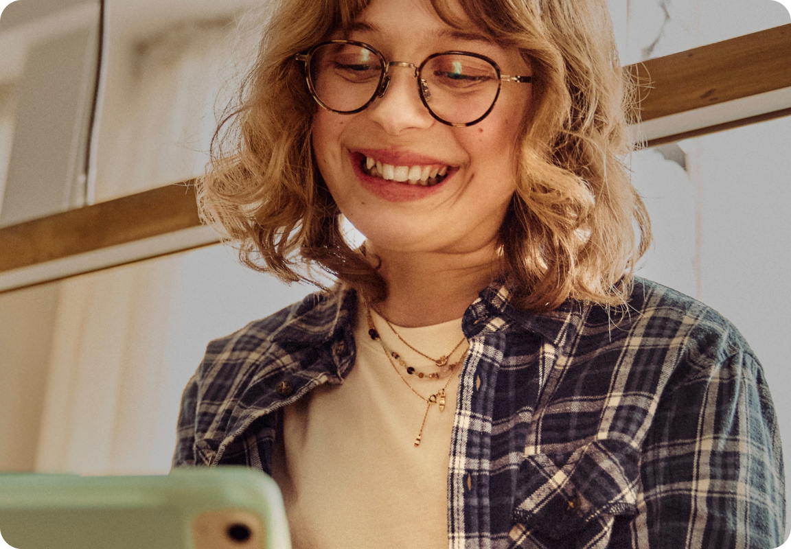 Smilende person med briller bruger mobiltelefon i hyggelige og lyse omgivelser.