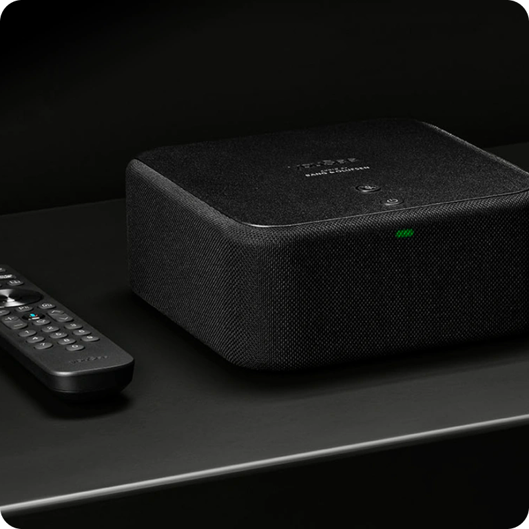 YouSee Audio og fjernbetjening placeret på mørk overflade i stilrent produktfoto.